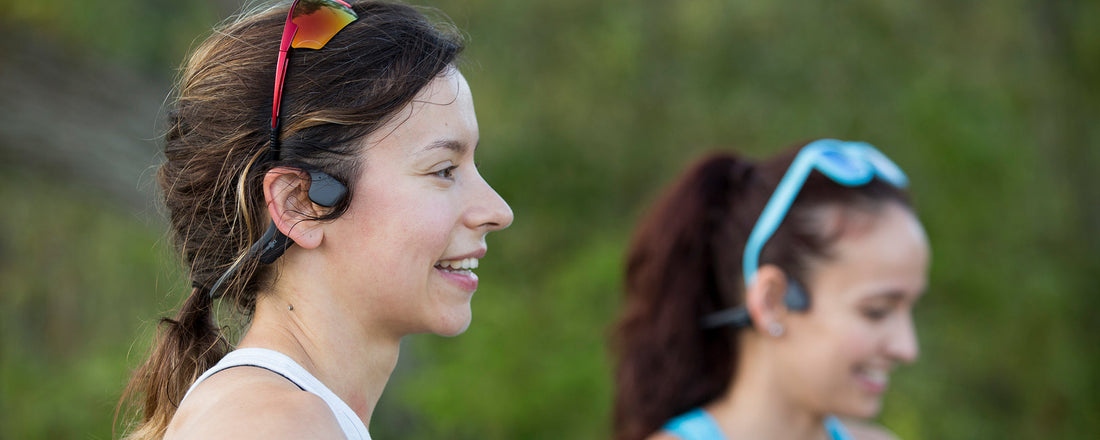 Two women wearing AfterShokz headphones with sunglasses
