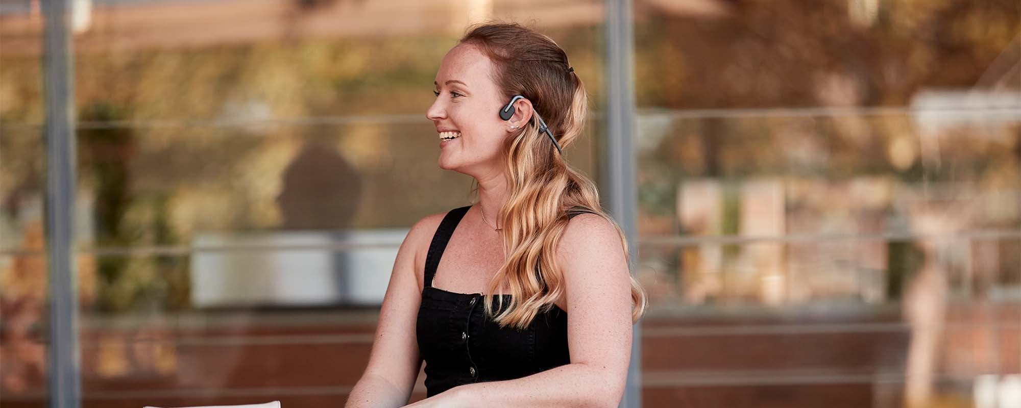 Woman sitting outdoors wearing AfterShokz Aeropex wireless headphones