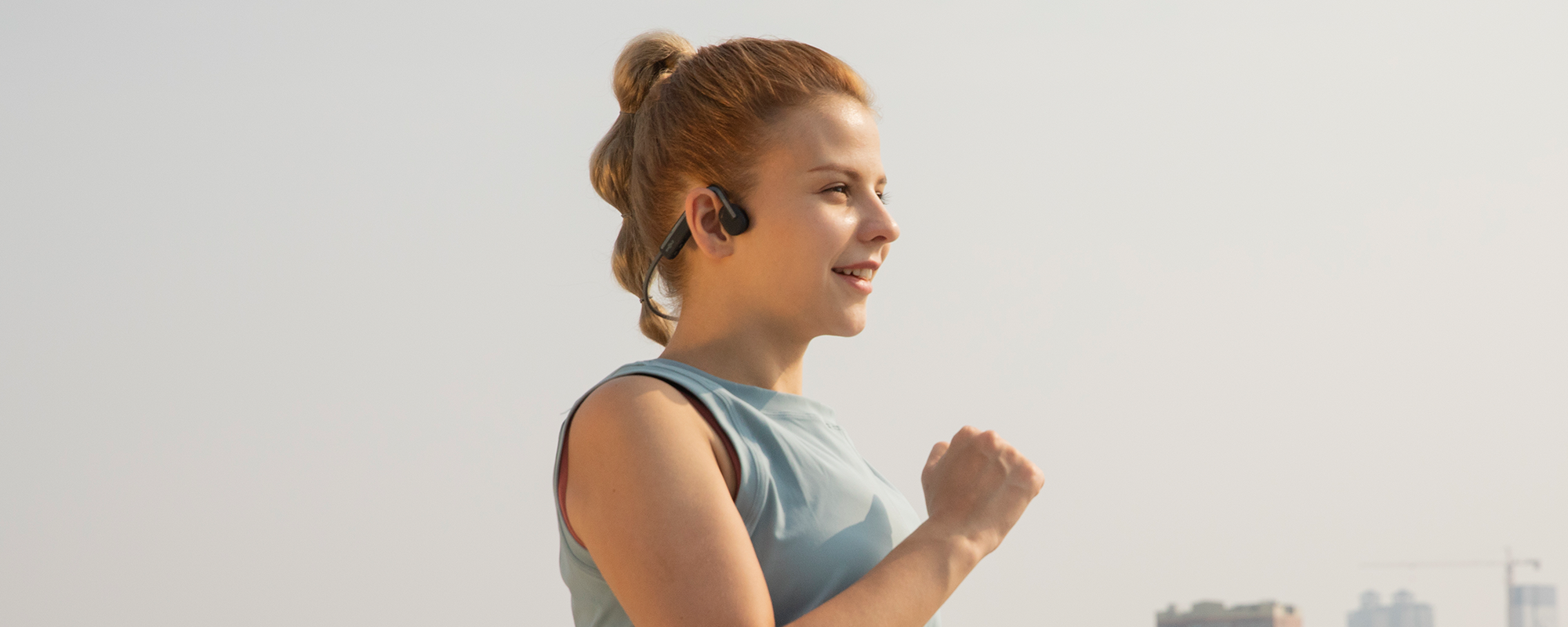Woman running outdoors wearing Shokz open-ear wireless headphones
