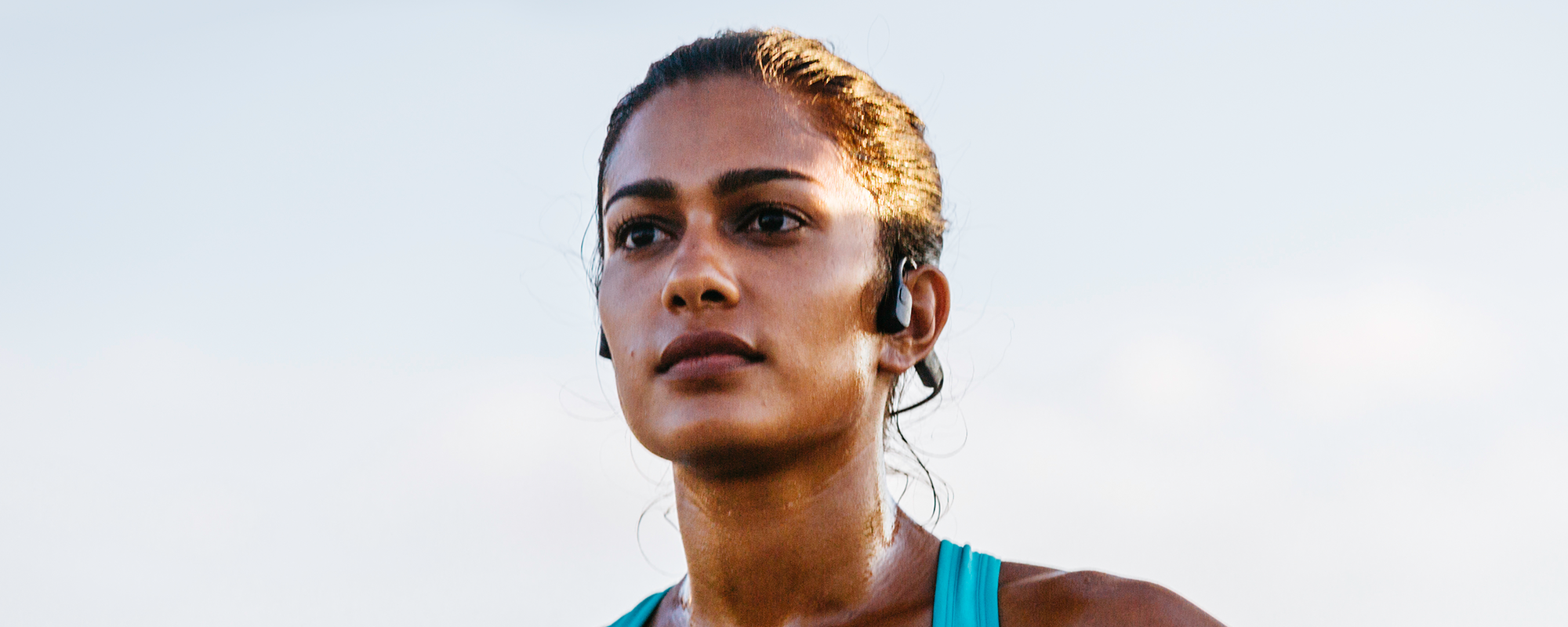 Close up image of woman running outdoors and wearing Shokz OpenRun sports headphones