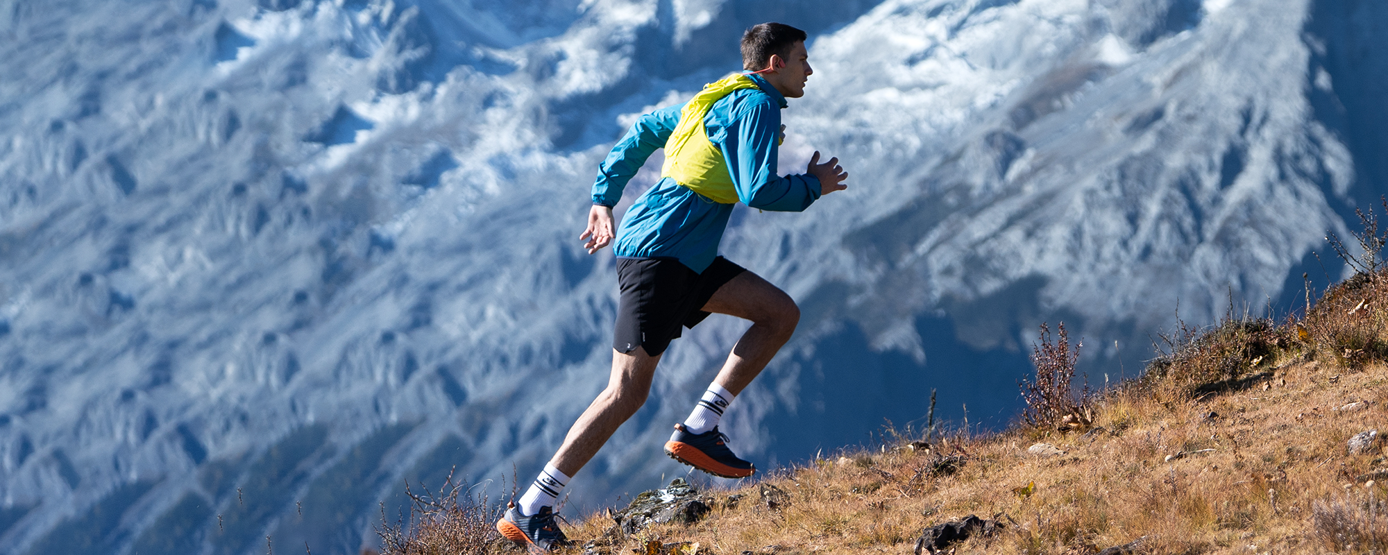 Image of a man running uphill outdoors in a mountain range while wearing Shokz OpenRun Pro wireless headphones