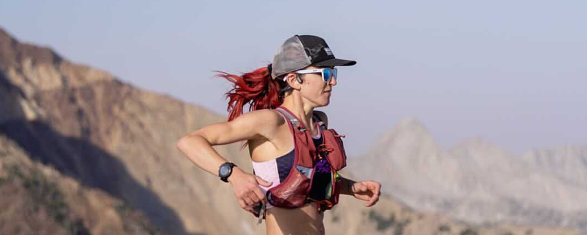 Professional Trail Runner & Coach Amanda Basham running with weighted vest down mountainside wearing OpenRun Pro open-ear headphones