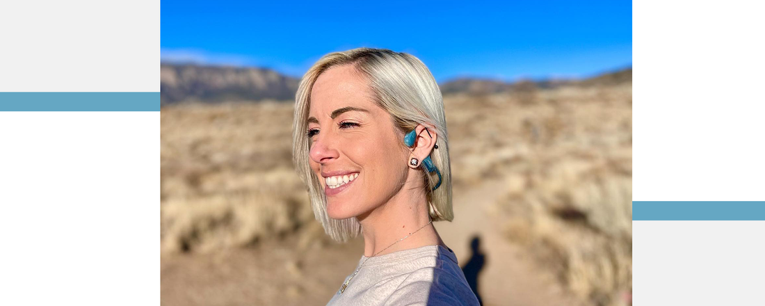 Woman outside smiling and wearing blue Shokz OpenRun Pro wireless sport headphones