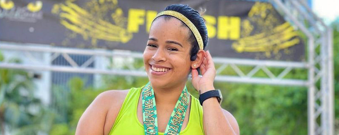 Woman wearing race medal and AfterShokz wireless headphones