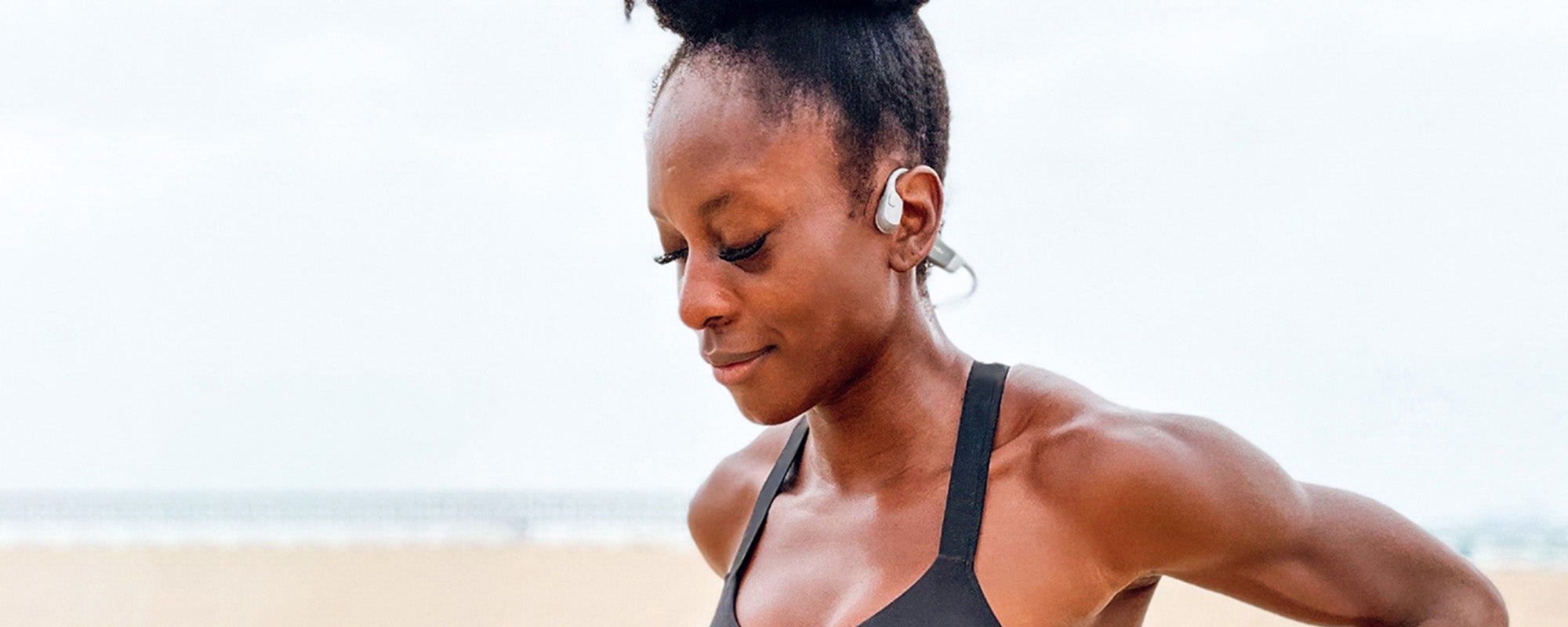 Close-up image of Millie Sam-Otuh at the beach wearing Shokz OpenRun wireless headphones