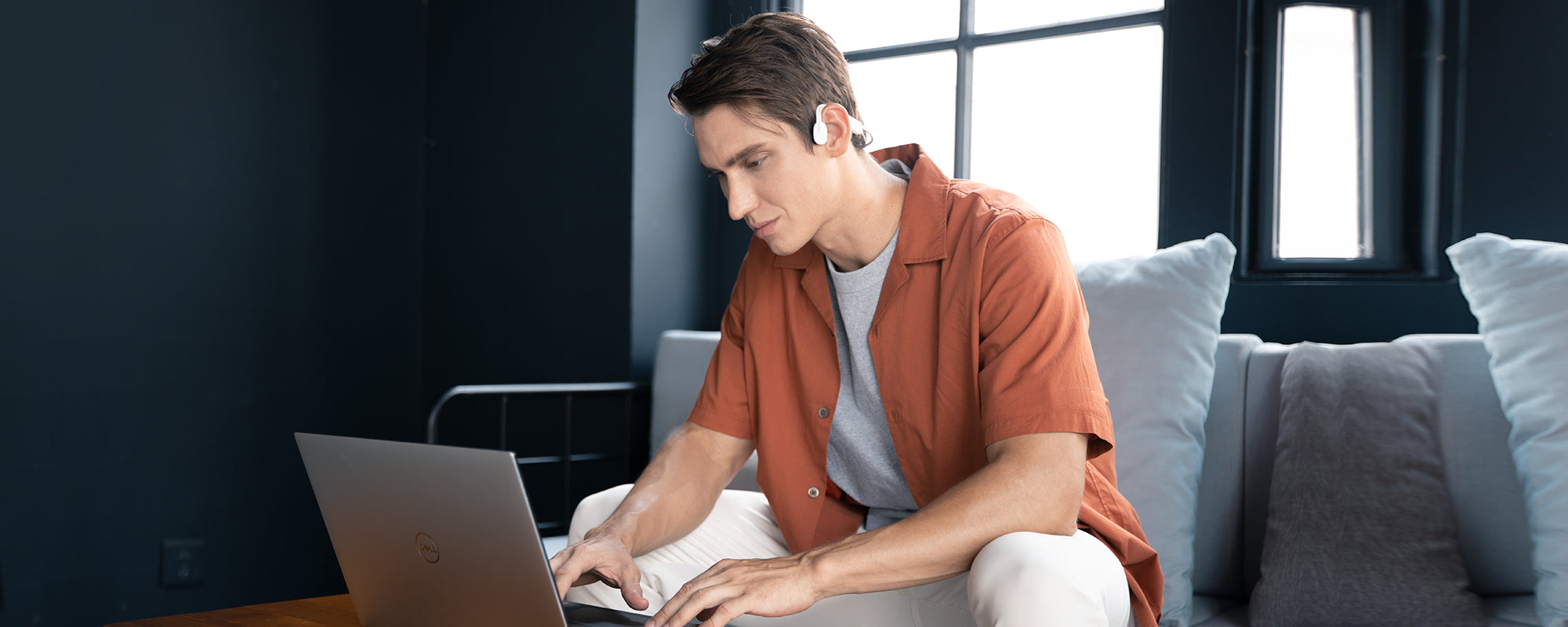 Man on laptop while wearing AfterShokz OpenMove headphones