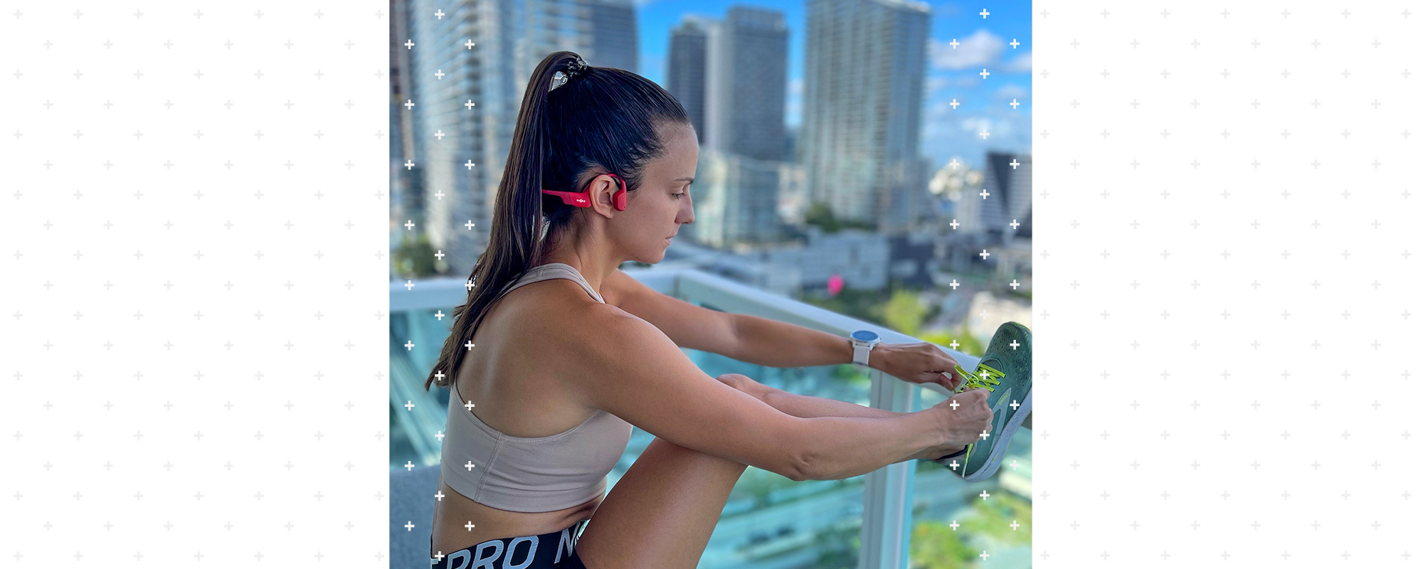 Woman standing on balcony doing leg stretches while wearing Shokz OpenRun wireless headphones